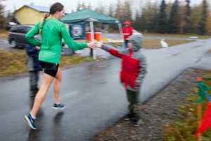 Photo by Rashah McChesney/Peninsula Clarion  Joann Jeplawy takes a cup of water from Samuel Anders at a relay station on the the Kenai River Marathon route along the Kenai Spur Highway on Sunday Sept. 26, 2015 in Kenai, Alaska. Jeplawy finished 18th out of the 97 runners in the half marathon race.