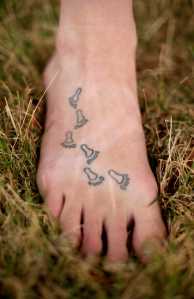 In this photo taken Aug. 28, 2015, Bethany Hughes shows six tattooed footprints on her foot that represent countries she has lived in. Growing up with missionary parents has fostered a wandering spirit in Hughes, who plans to spend five years in an attempt to become the first woman to trek from the southern tip of South America to the northern tip of Alaska all by non-motorized means. (AP Photo/Charlie Riedel)