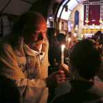 In this Nov. 18, 2015 photo, the Rev. Scott Fisher hands a Baptism candle to Aiden Taylor during a service at St. Matthew's Episcopal Church in Fairbanks, Alaska. With long hair, unruly sideburns and colorful Converse sneakers, Fisher is known to many as the "hippy" priest. (Eric Engman/Fairbanks Daily News-Miner via AP)