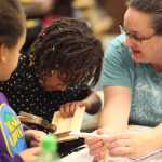 Photo by Kelly Sullivan/ Peninsula Clarion (Left) Fourth grader Ruthie Davis watches her sister, second grader Ginjer Davis, use a hammer for the first time during the Bites for Birds event, where Title I students were invited to learn how to make birdhouses with their parents after school Thursday, Dec. 3, 2015, at Mountain View Elementary School in Kenai, Alaska. The girls' mother Carmen Wright said it was hard to let her younger daughter take the reins during the project's construction phase.