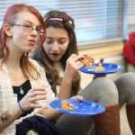 Photo by Kelly Sullivan/ Peninsula Clarion Two members of the Granny Wannabees, Nikiski-Middle High School's middle school knitting club, munch on pizza after the group officially presented their handmade blankets to staff from the Nikiski Senior Center Thursday, Dec. 10, 2015, in the school's library in Nikiski, Alaska.