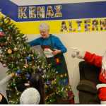 Photo by Megan Pacer/Peninsula Clarion Susan Smalley helps re-erect a tree that fell during Kenai Alternative High School's annual Grinch Day celebration while her husband, Hal Smalley, poses as Santa Clause on Thursday, Dec. 17, 2015 at the school in Kenai, Alaska. Hal Smalley presented each student with a hand-made pillow case full of treats as a send off to their winter break.
