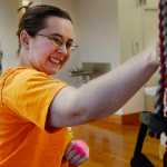 Ben Boettger/Peninsula Clarion Nicole Harmon reaches for a resistance band she will use in a rowing exercise, part of her physical therapy, on Thursday Dec. 10 at the Dena'ina Wellness Center in Kenai. Harmon's physical therapist Sabrina Royster said the exercise is "meant to help her brain re-educate the muscles of her arm to balance muscle contractions. "