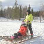 Photo by Megan Pacer/Peninsula Clarion Sophie Tapley relaxes in a sleigh while her older sister Mercedes Tapley rides along behind as they are pulled around an enclosure by a horse on Monday, Feb. 8, 2016 at Alaska C&C Horse Adventures in Soldotna, Alaska.