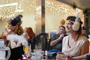 Jodi Crandall (left) and Heidi Meeham listen to comedian Dave Burroughs during a "Roaring '20s" themed dinner and comedy show charity event on Saturday, Feb. 13 at the Kenai Senior Center. The event, hosted by the Kenai Peninsula Association of Realtors, raised money for Habitat for Humanity and Hospice of the Central Peninsula.