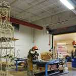 Photo by Elizabeth Earl/Peninsula Clarion Cam Choy, an assistant professor of art at Kenai Peninsula College, cuts through a bar of steel in the college's 3D design studio on Friday, April 15, 2016. He welds the steel into sculptures like the figure seen at left.