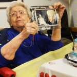 Photo by Megan Pacer/Peninsula Clarion Hazel George opens a present - side-by-side photos of her as a baby and in the present - during a birthday party Sunday, April 24, 2016 at Heritage Place in Soldotna, Alaska. George joined the other centenarians in the state when she turned 100 Sunday.