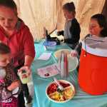 Ginni DeLon hands her daughter a glass of lemonade she bought from Charisma Watkins (left) and Valerie Cazares, who offered free fruit at their stand on Saturday, June 11 in Kenai. DeLon said she traditionally brings her children to all the lemonade stands in town on Lemonade Day.
