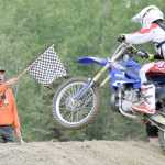 Photo by Joey Klecka/Peninsula Clarion Kenai Peninsula Racing Lions flagman Phil Celtic shows the checkered flag to Kraig Riese in Saturday's 250cc Expert division.