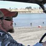 Photo by Elizabeth Earl/Peninsula Clarion Jason Floyd, the owner of Ammo Can Coffee, drives a side-by-side on the south beach of the Kenai River on Monday, July 18, 2016 in Kenai, Alaska. Floyd parked a trailer serving coffee near the entrance to the personal use dipnet fishery and makes delivery runs along the beach, selling ice and taking coffee orders.