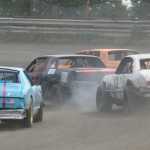 Photo by Joey Klecka/Peninsula Clarion Mike Craig (middle) races through the third turn Saturday at Twin City Raceway in Kenai with Sean Ensley (orange car), Dean Scroggins (13) and Amy Hermanns.
