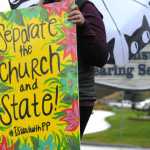 Photo by Elizabeth Earl/Peninsula Clarion Kyra Bodnar holds a hand-painted sign near where members of the Catholic Church gathered to pray near the Kenai Peninsula Borough Administration Building on Wednesday, Aug. 17, 2016 in Soldotna, Alaska. The church members decided to pray outside the borough administration building after a Satanic invocation was given to open the borough assembly meeting Aug. 9.