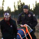 Photo by Megan Pacer/Peninsula Clarion Evan Butcher, a member of the Kenai River Brown Bears hockey team, helps a Kenai firefighter carry a volunteer victim on a stretcher to safety during a mass casualty drill Tuesday, Oct. 11, 2016 at the Kenai Municipal Airport in Kenai, Alaska. The airport is required by the Federal Aviation Administration to hold the drill every three years to test its emergency planning.
