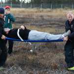 Photo by Megan Pacer/Peninsula Clarion Kenai Fire Battalion Chief Tony Prior and a Kenai firefighter carry a volunteer pretending to be an injured plane crash victim to safety on a stretcher during a mass casualty drill Tuesday, Oct. 11, 2016 at the Kenai Municipal Airport in Kenai, Alaska. The airport is required by the Federal Aviation Administration to hold the drill every three years to test its emergency planning.