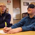 Ben Boettger/Peninsula Clarion Jessica Croom (left) serves as a sighted helper to blindfolded Tristan Arnold, making a drawing during River City Academy's Blindness Challenge on Thursday, Oct. 13 in Soldotna. After trying to draw and write on regular paper, the blindfolded students  used swell paper, which absorbs ink and expands, creating raised lines that a blind artist can feel.