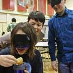 Ben Boettger/Peninsula Clarion Blindfolded Kaegan Koski eats lunch in the River City Academy cafeteria/gym, while fellow students Aiden Huff and blindfolded Tristan Arnold stand behind him on Thursday, Oct. 13 in Soldotna.