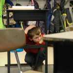 Photo by Megan Pacer/Peninsula Clarion Mountain View Elementary second grader Blake Kinsley, 7, crouches under his desk with his head covered during this year's Great Alaska ShakeOut earthquake drill Thursday, Oct. 20, 2016 at the school in Kenai, Alaska.