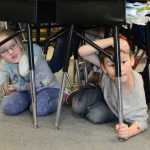 Photo by Megan Pacer/Peninsula Clarion Mountain View Elementary second graders Elsa Meyer, 7, and Devin Seaton, 7, wait under their desks with their head and necks covered during this year's Great Alaska ShakeOut earthquake drill Thursday, Oct. 20, 2016 at the school in Kenai, Alaska.
