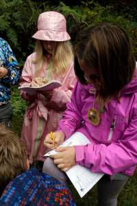 In this Oct. 6, 2016 photo, Outdoor School students Maya Herring, left, and Evie Larson enter notes in their field study notebooks during a lesson at Camp Howard in Mount Hood National Forest near Corbett, Ore. The outdoor education is unique to Oregon and is a rite-of-passage for public school students that's meant to instill a respect for nature in each generation - studies show it improves attendance and boosts test scores. (AP Photo/Don Ryan)