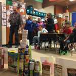 Students in Kellie Davidson's class at Redoubt Elementary School in Soldotna watch as judges evaluate their Christmas Wall, built using food items brought in by students for the school's "Canstruction" competition Thursday. Food items collected during the event will be donated to the Kenai Peninsula Food Bank. (Photo by Will Morrow/Peninsula Clarion)