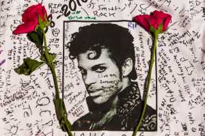 FILE - In this April 22, 2016 file photo, flowers lie on a T-shirt signed by fans at a makeshift memorial for musician Prince outside the Apollo Theater in New York. The singer died April 21, 2016, at the age of 57. With the loss of several icons of Generation X's youth, the year 2016 has left the generation born between the early 1960s and the early 1980s, wallowing in memories and contemplating its own mortality. (AP Photo/Andres Kudacki, File)