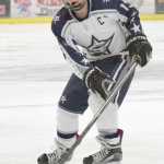 Photo by Joey Klecka/Peninsula Clarion Hutchison goaltender Zach Baxter dives to cover the puck in front of a charging Matthew Daugherty (5) Friday night at the Soldotna Regional Sports Complex.
