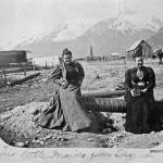 Two little maids from Skagway looking southwest down Main Street, circa summer 1898. Mollie Brackett, left, and Mrs. Tuckerman sit on a wood stave pipe, which was about to be installed on Main Street, possibly at the cross street of 3rd Ave. Tuckerman is holding a woodbox camera probably similar to the one Brackett used. (Courtesy Photo | National Park Service, Klondike Gold Rush National Historical Park, Brackett Family Collection, BRSGY089, KLGO SP-143-5368)