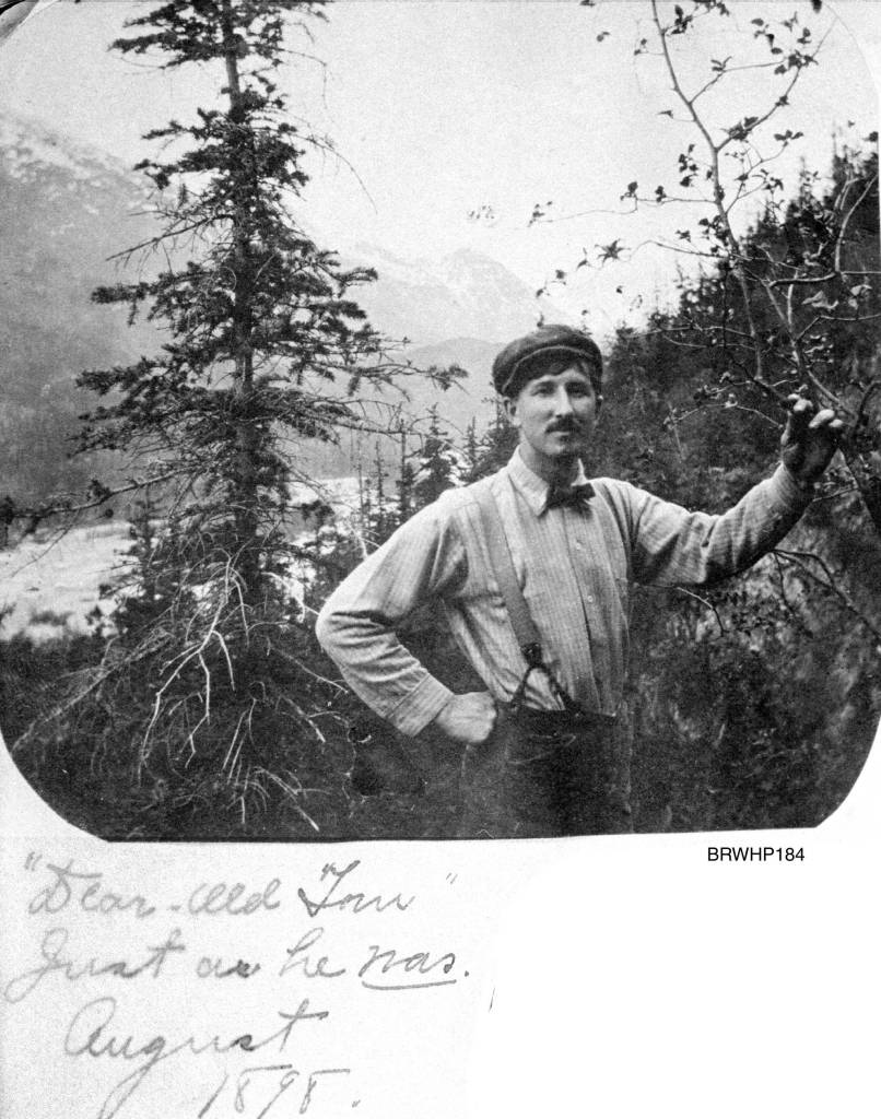 Dear old Tom just as he was looking southeast, circa August 1898. Tom Brackett standing on the west side of the Skagway River Valley with the valley floor below and the mountains surrounding Skagway behind him. Tom Brackett died of Typhoid fever on Feb. 26, 1901 in Portsmouth, New Hampshire. This note indicates that Mollie Brackett probably assembled her album sometime after Toms death. (Courtesy Photo | National Park Service, Klondike Gold Rush National Historical Park, Brackett Family Collection, BRWHP184, KLGO WP-23-5366.)