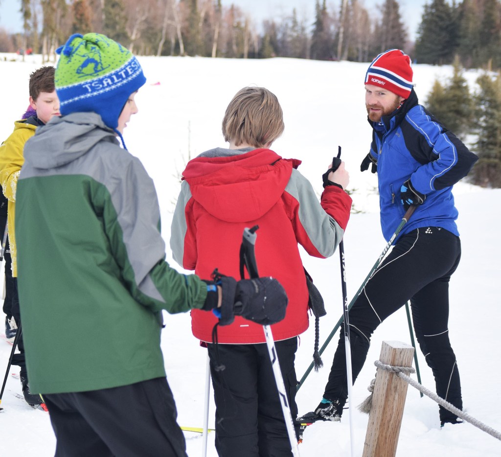 Tsalteshi Trails Youth Ski Program coach Darin Markwardt (red hat) quizzes a group of young skiers, Jan. 28 at the Kenai Golf Course. (Photo by Joey Klecka/Peninsula Clarion)
