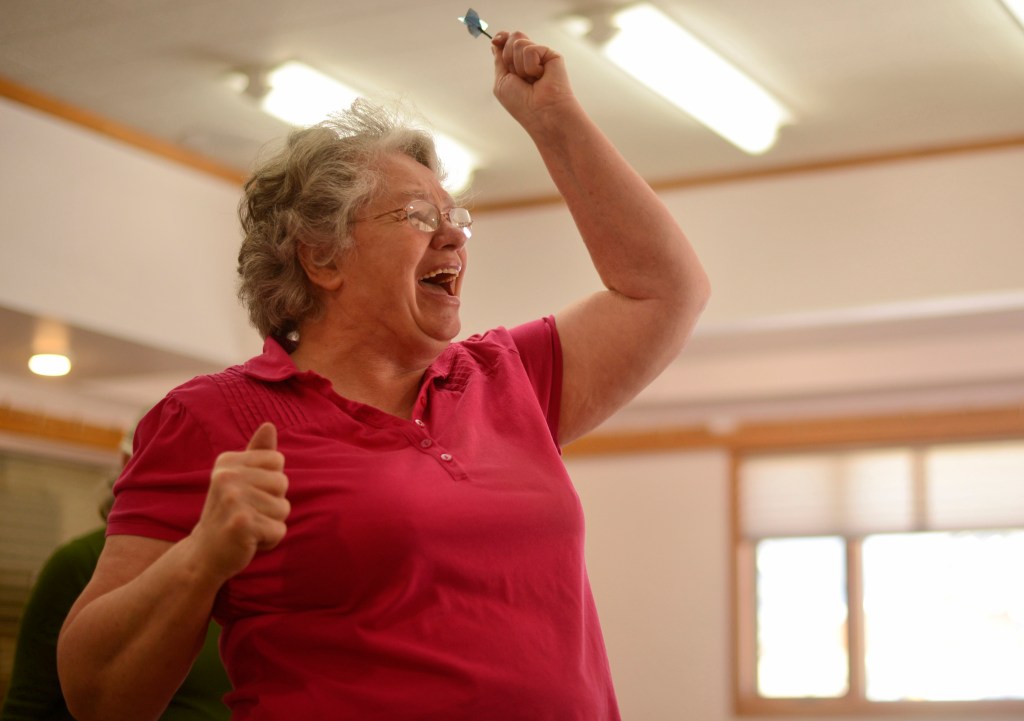 Bonnie Cain, an organizer of the 13th annual Kenai Peninsula Senior Olympics, reacts after scoring a hit during the Senior Olympics darts competition on Wednesday, Feb. 22, 2017 at the Soldotna Senior Center in Soldotna, Alaska. The competition was the first time Cain had played darts. &ldquo;They talked me into it,&rdquo; she said, of the friends playing with her.