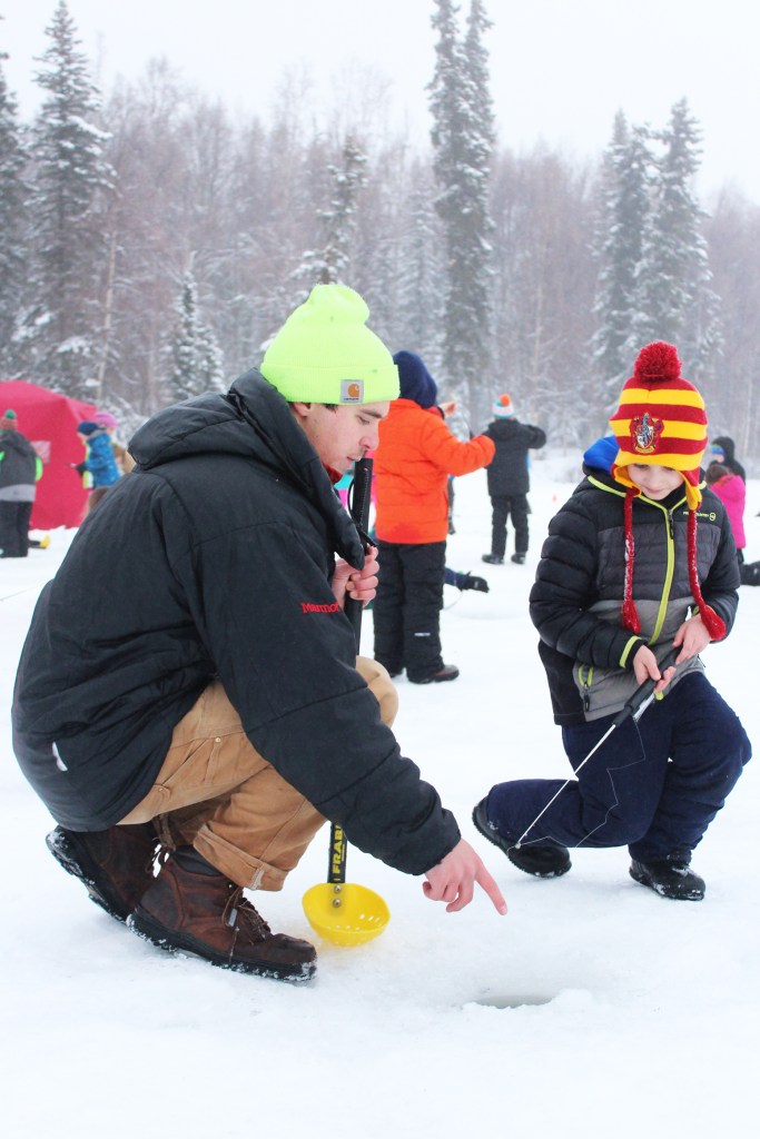 Environmental scientist Jeff Sires with the Kenai Watershed Forum lends a hand to 9-year-old Carson Grimm, a fourth grader at Kaleidoscope School of Arts and Sciences, during an ice fishing outing Friday, Feb. 24, 2017 on Sport Lake in Soldotna, Alaska. Sires was one of several volunteers helping with Friday's outing, which is one of three put on each year by the Alaska Department of Fish and Game as part of its "Salmon in the Classroom" program that several schools throughout the Kenai Peninsula Borough School District participate in. (Megan Pacer/Peninsula Clarion)