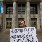 Bradley Johnson, a state employee at the Department of Revenue, holds his protest sign during noon rally against the Legislature&rsquo;s lack of a budget compromise on Thursday, June 22, 2017. (Michael Penn | Juneau Empire)