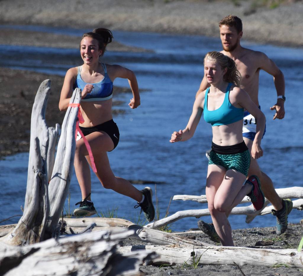 From left to right, Riana Boonstra, Alex Bergholtz and Josiah Martin leap several beached logs Saturday at the third annual Clam Scramble Mud Run in Ninilchik. (Photo by Joey Klecka/Peninsula Clarion)