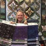Dana Woodard holds up a selection of her newly designed fabric collection in front of a quilted pattern on display, and for sale, at Kenai Fabric Center. (Photo courtesy Gwen Woodard)