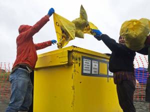 Karl Danielson (left), a senior at Kenai Central High School and a member of the KCHS Cross Country Ski Team, his mom Teresa Danielson (center) and coach Brad Nyquist (right) empty out their garbage bags into a bin at the north Kenai Beach on Tuesday, July 18, 2017 in Kenai, Alaska. Members of the ski team helped clean up the beach Tuesday as a fundraiser for the team&rsquo;s activities. (Photo by Elizabeth Earl/Peninsula Clarion)