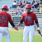 Isaac Deveaux (14) gives Peninsula Oilers teammate Kellen Strahm a low five after Strahm scored a run against the Chugiak Chinooks, Saturday afternoon at Coral Seymour Memorial Ballpark in Kenai. (Photo by Joey Klecka/Peninsula Clarion)