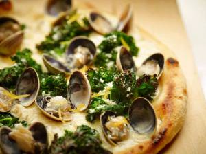 This June 2 photo provided by The Culinary Institute of America shows a grilled white pizza with cockles, lemon and kale. This dish is from a recipe by the CIA. (Phil Mansfield/The Culinary Institute of America via AP)