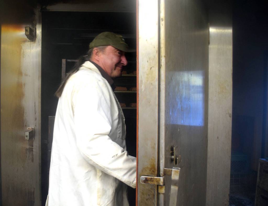 Left: In a haze of smoke, Fred West, owner of Tustumena Smokehouse, opens the door to the smoker where a batch of Kylee&rsquo;s Alaska Salmon Bacon is smoking.