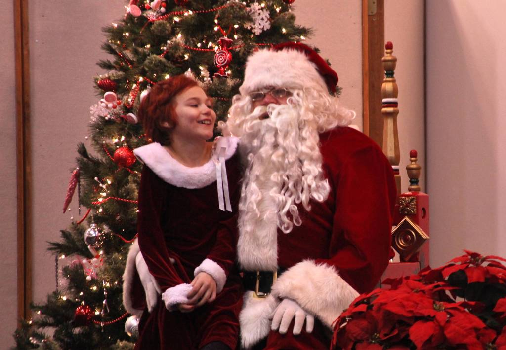 Haylee Bush poses for a photo with Santa Claus, who is a close friend of Kenai City Councilman Tim Navarre, in her favorite Christmas dress on Friday at the Kenai Visitor&rsquo;s Center. (Photo by Ben Boettger/Peninsula Clarion)