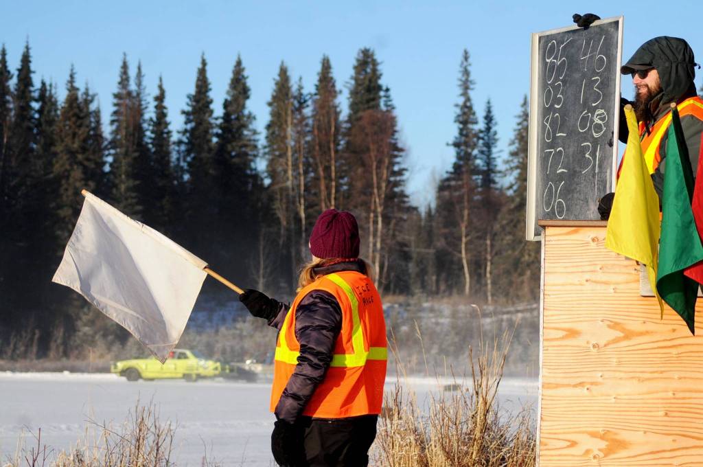 Michael Hutton (right) and Robin Wylie signal racecar drivers with flags as drivers skid around one of the corners on the ice track atop a frozen lake at the Decanter Inn on Sunday, Jan. 22, 2018 in Kasilof, Alaska. Every Sunday in the winter, the Decanter Inn hosts Peninsula Ice Racing events for drivers to try their hand at the frozen track on the shallow lake at the bottom of the hill behind the inn. The racers can use studded tires on their front wheels only and equip the sides of their vehicles with bumpers as other vehicles are likely to slip and slide into them. Spinning out is common. A tow truck waits on the sidelines to retrieve drivers who get stuck on the berms alongside the track. Fans gathered Sunday despite the cold to cheer the racers on. The men race in the morning, followed by the women&rsquo;s races in the afternoon. (Photo by Elizabeth Earl/Peninsula Clarion)