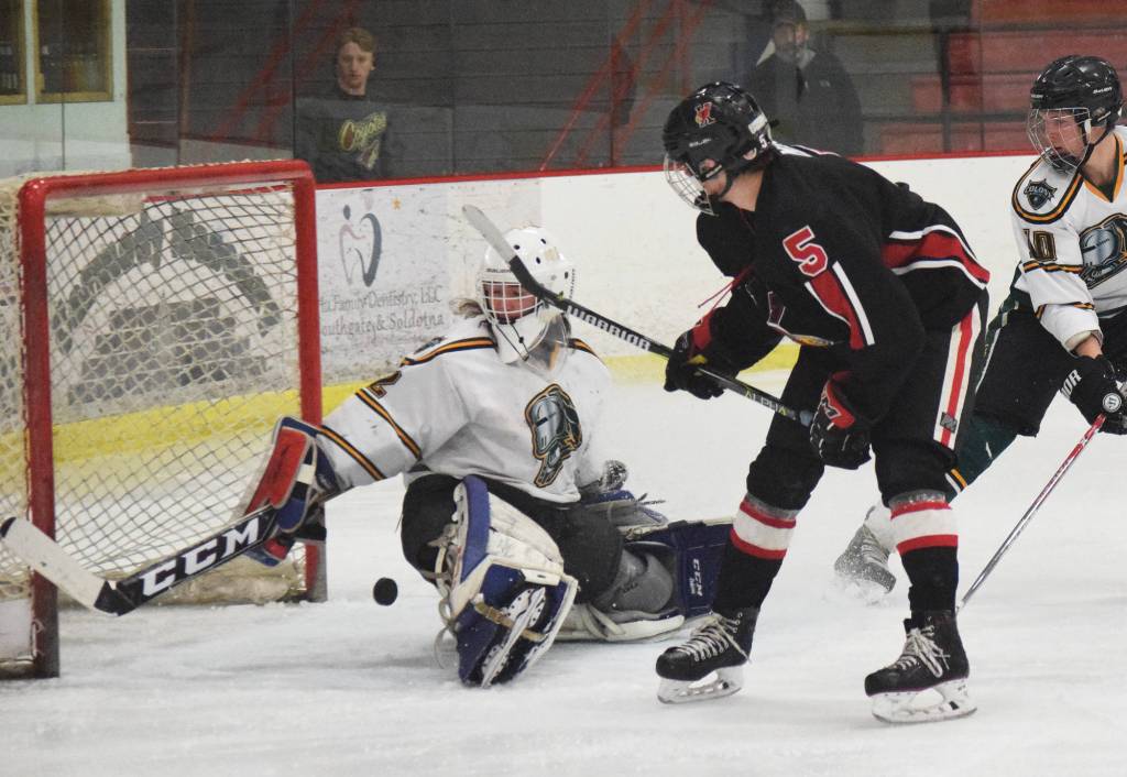 Kenai Central skater Levi Mese (5) watches as the puck nearly slips by Colony goalie Cole Doss, Friday in a North Star Conference tournament semifinal at the Soldotna Regional Sports Complex. (Photo by Joey Klecka/Peninsula Clarion)