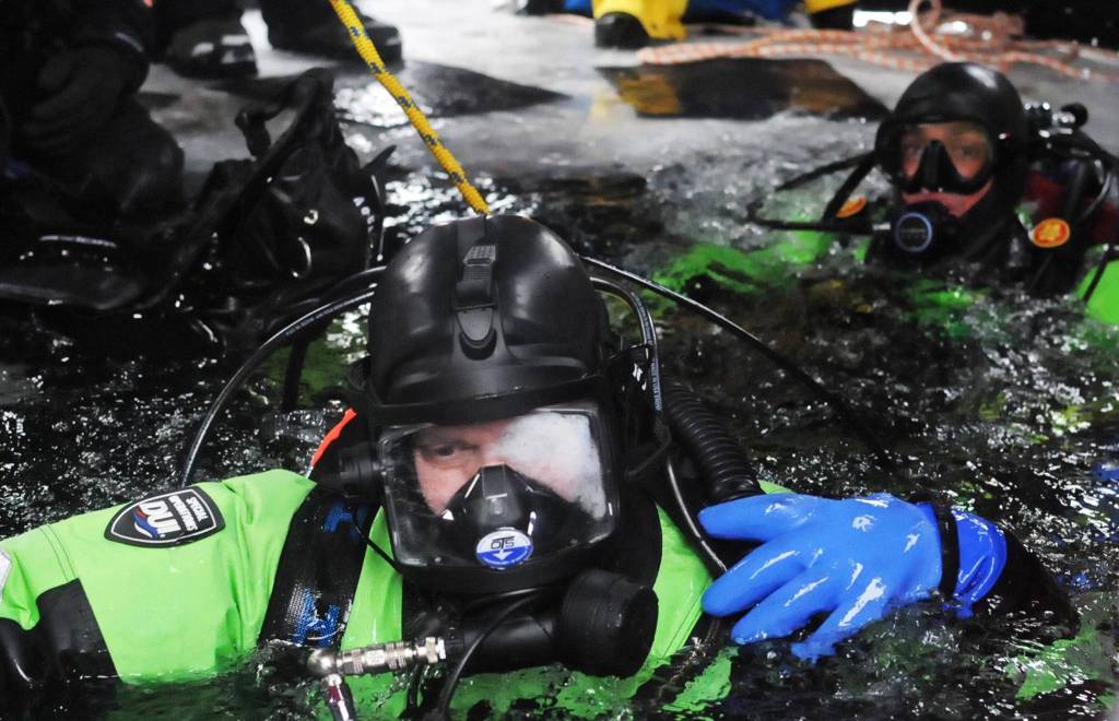 Matt Quiner (left) and Kassidy Stock (right) of the Nikiski Fire Department prepare to dive through a hole in the ice on Island Lake as part of a diving training drill Friday, March 9, 2018 in Nikiski, Alaska. The Nikiski Fire Department is working on getting its ice diving team up to certifications to perform operations on frozen lakes if need be, such as rescuing sunken cars or people or recovering evidence. (Photo by Elizabeth Earl/Peninsula Clarion)
