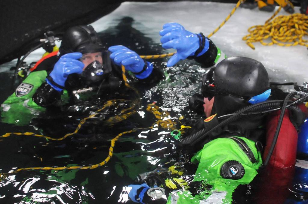 Kassidy Stock (right) of the Nikiski Fire Department signals diving partner Matt Quiner (left) to dive through a hole in the ice on Island Lake as part of a diving training drill Friday, March 9, 2018 in Nikiski, Alaska. The Nikiski Fire Department is working on getting its ice diving team up to certifications to perform operations on frozen lakes if need be, such as rescuing sunken cars or people or recovering evidence. (Photo by Elizabeth Earl/Peninsula Clarion)