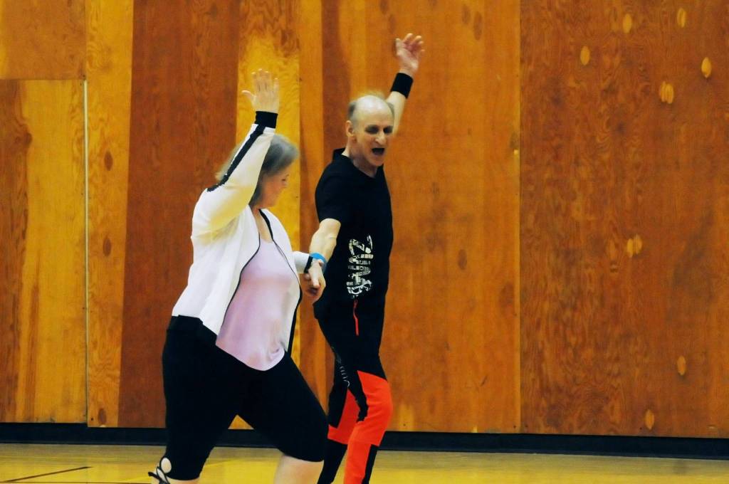Zumba instructor Truman Krogel takes a few dance steps with a student during a Zumba Gold class at the Kenai Recreation Center on Thursday, March 15, 2018 in Kenai, Alaska. Krogel, 74, said he first tried Zumba himself four years ago, loved it and began teaching classes of his own in January 2017. (Photo by Elizabeth Earl/Peninsula Clarion)