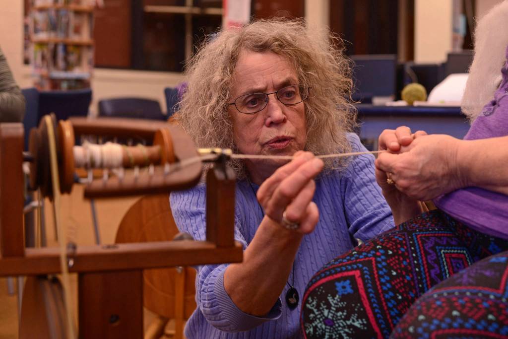 Instructor Lee Coray-Ludden (center) inspects yarn from a kick-driven spinning wheel on Tuesday in the Soldotna Preparatory School library in Soldotna. In her four-session weekly yarn spinning class, part of the Soldotna Community Schools program, Coray-Ludden will teach students to spin and ply yarn from locally-grown wool and fleece, including exotic fibers from cashmere goats, alpacas, and llamas. (Photo by Ben Boettger/Peninsula Clarion).