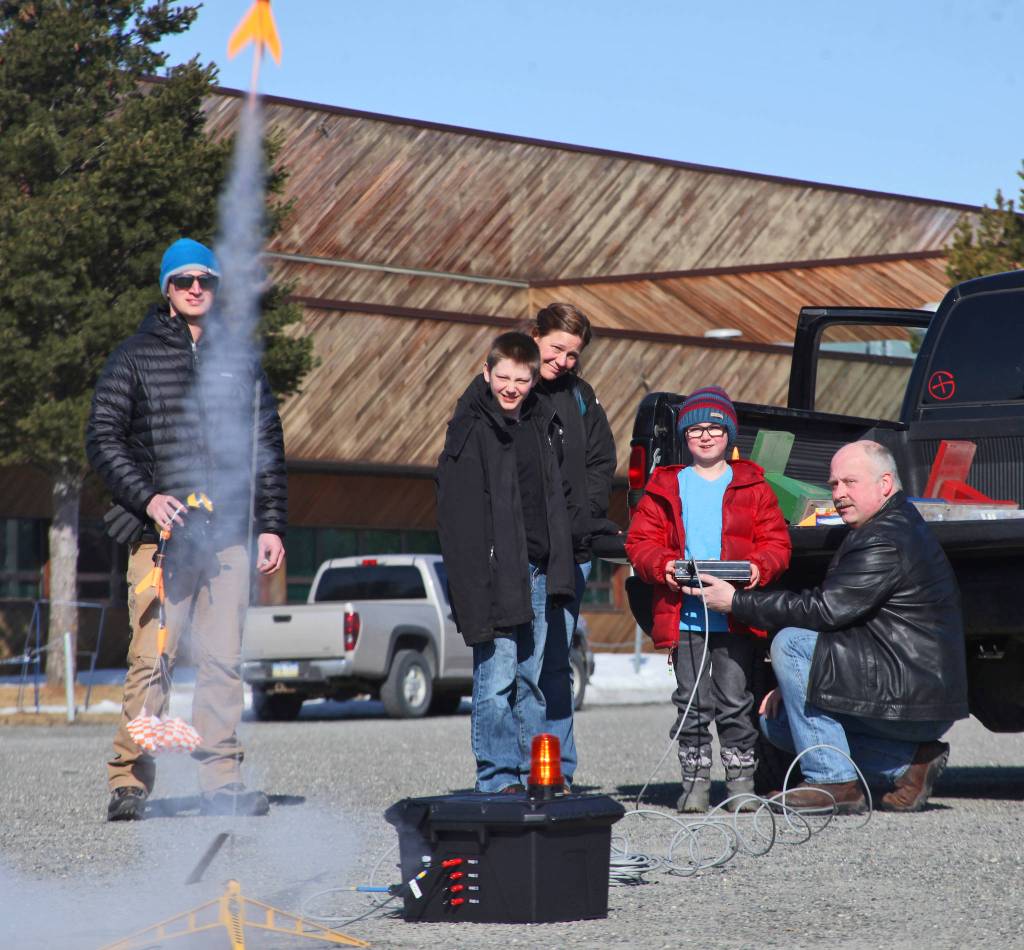 With the push of a button, Owen Walsh (in red) sends a model rocket into the sky, as instructor Scott Aleckson (right) and other students of his rocketry class watch in the parking lot of the Soldotna Regional Sports Complex in Soldotna on Saturday. Aleckson said he made and launched his first plastic, balsa wood, and cardboard rocket as a 4th grade student at Soldotna Elementary School. Since then he&rsquo;s built a custom launch system, he said, &ldquo;with recycled electronics and a lot of soldering time.&rdquo; Aleckson taught Saturday&rsquo;s rocketry class through the Soldotna Community Schools program, and would like to continue spreading the hobby. &ldquo;If I could get a model rocket club going, that&rsquo;d be great,&rdquo; he said. &ldquo;Stuff like this is much more fun in a group.&rdquo; (Photo by Ben Boettger/Peninsula Clarion)