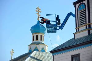 Glenn Beckmann of Rainproof Roofing inspects a weathered and tilting cross atop Kenai&rsquo;sHoly Assumption of the Virgin Mary Russian Orthodox Church before removing it on Friday, May 4, 2018. Dorothy Gray , a Holy Assumption member and treasurer of the preservation nonprofit Russian Orthodox Sacred Sites in Alaska, said the church is now looking for local craftspeople interested in making replacements for the three old crosses. (Ben Boettger/Peninsula Clarion)