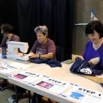 Lori Landstrom, left, and Tara Riemer, right, of Sustainable Seward create reusable shopping bags out of donated shirts during the Seward Music and Arts Festival on Sunday. Sustainable Seward is a grassroots organization working to raise awareness and implement solutions for waste reduction and recycling in the Seward area. (Photo by Kat Sorensen/Peninsula Clarion)