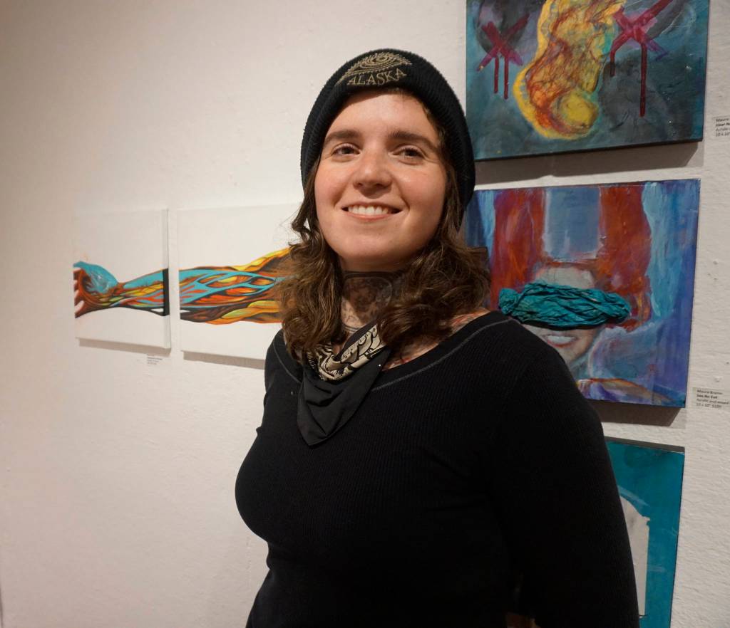 Sarah Frary stands by her paintings, Anatomical Landscape, left, at the First Friday, Dec 7, 2018, opening of Bunnell Street Arts Centers 10x10 show in Homer, Alaska. (Photo by Michael Armstrong/ Homer News)