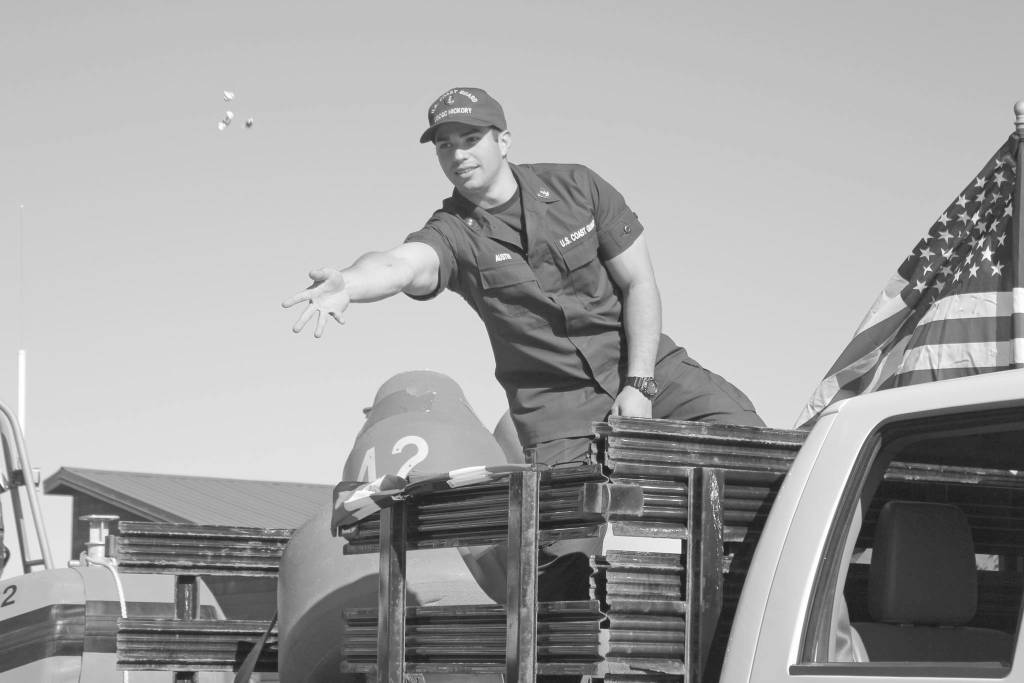 A member of the U.S. Coast Guard tosses candy to children and families lining Pioneer Avenue during the annual Independence Day parade July 4, 2018 in Homer. (Photo by Megan Pacer/Homer News)